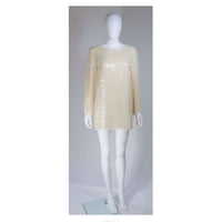 This Oleg Cassini tunic is composed of an off-white iridescent sequined silk. Features side slits with white beading embellishment, there is a center back zipper closure. In great vintage condition. 
