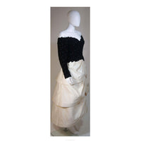 This Arnold Scaasi Couture gown is composed of a black velvet bodice fabricated from floral cut-outs and an off white tiered silk satin skirt. The gown has an off the shoulder style design with sweetheart neckline. There is a center back zipper closure and zippers at the sleeve end. In excellent vintage condition. 