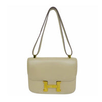 HERMES Camel Constance Crossbody Bag. This Hermes leather bag features a gold H closure, gold hardware, and a bone top stitch. Made in France. Measurements in Inches: Length: 9 Height: 7 Width: 2 Strap single: 32 Strap doubled: 19