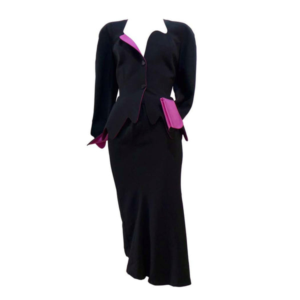 THIERRY MUGLER Black with Pink Lining and Cuff Skirt Suit Size 40. This THIERRY MUGLER skirt suit is composed of a black wool fabric with bright pink lining and cuff. Features a classic Mugler silhouette with nipped waist and curved bust-line to neckline design. The jacket has front snap closures, rounded shoulders, and a scalloped hem. The skirt features a zipper closure, flounce shape, and midi-length. In good vintage pre-owned condition. Made in France.Measurements in Inches:JacketBust: 40 Waist: 29 Skir